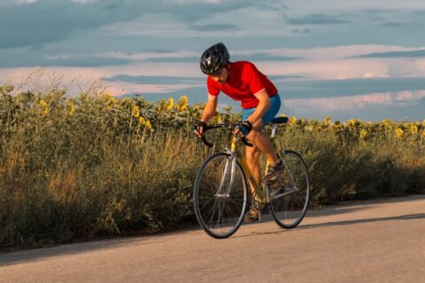 Man sprinting on his bike past a field of sunflowers