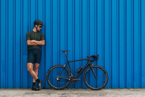 Man leans against a blue shipping container, looking at his all-black bicycle