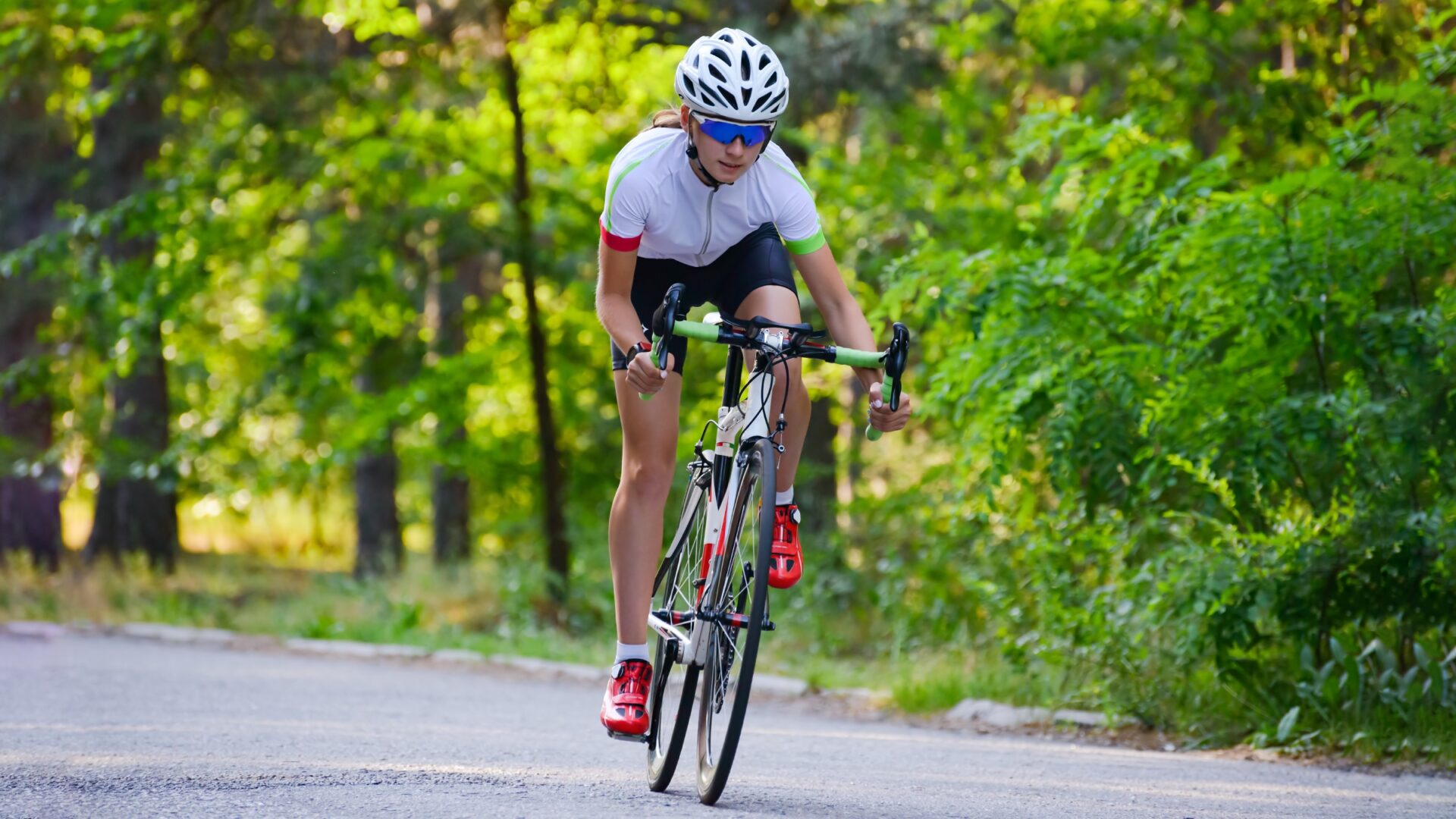 Woman riding her bike out of the saddle through a tree-lined road