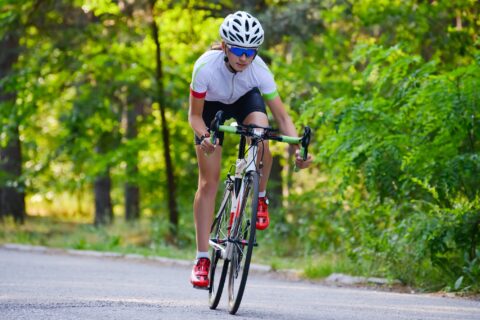 Woman riding her bike out of the saddle through a tree-lined road