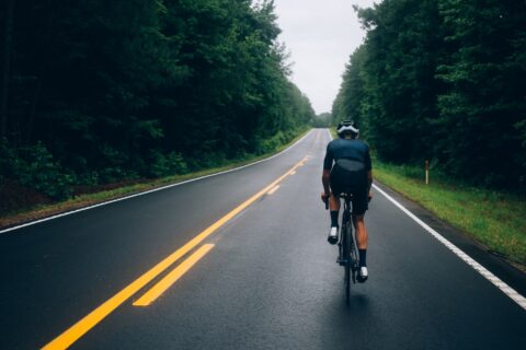 Rear shot of a cyclist riding alone along a tree-lined road on a rainy day