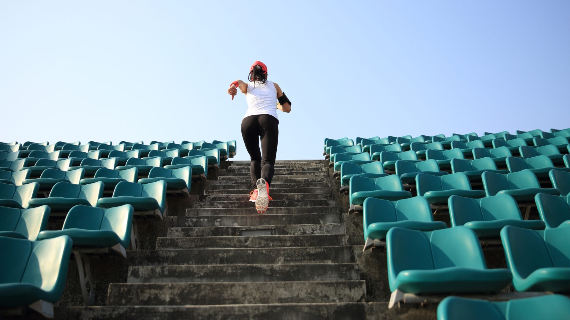 Rear view of a woman running up stairs at an outdoor stadium