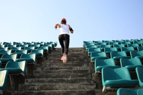 Rear view of a woman running up stairs at an outdoor stadium