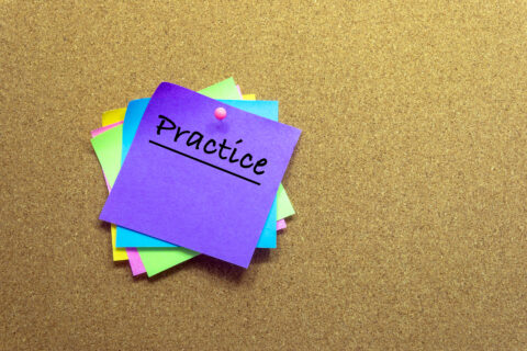 the word 'practice' on a post-it note on a wall. Practicing leads to performance gains.